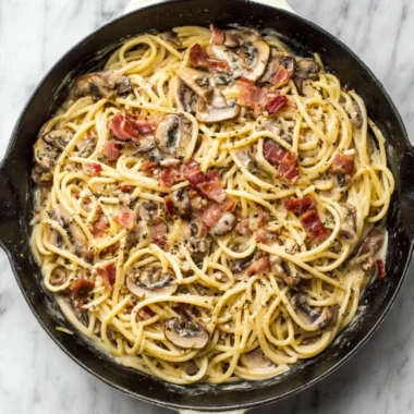 Bowl of creamy bacon mushroom pasta topped with herbs
