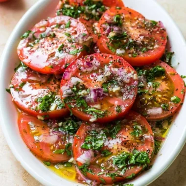 A bowl of marinated tomatoes garnished with herbs and spices.