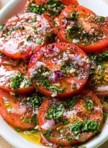 A bowl of marinated tomatoes garnished with herbs and spices.
