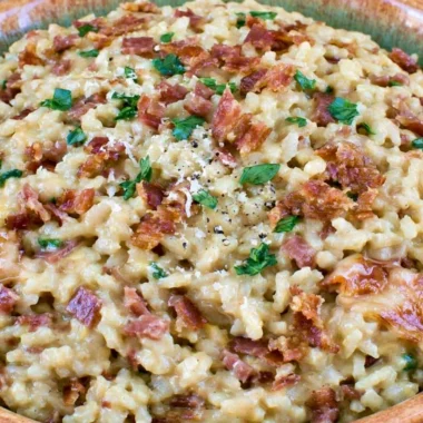 Creamy carbonara risotto garnished with herbs and cheese in a white bowl
