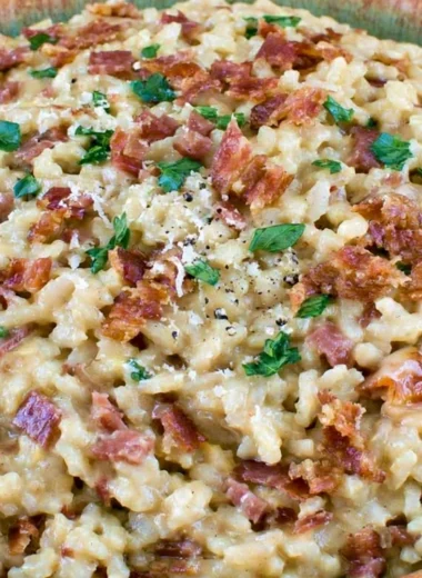 Creamy carbonara risotto garnished with herbs and cheese in a white bowl