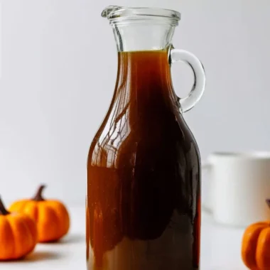 Pumpkin spice syrup bottle alongside a steaming cup of coffee and tea.