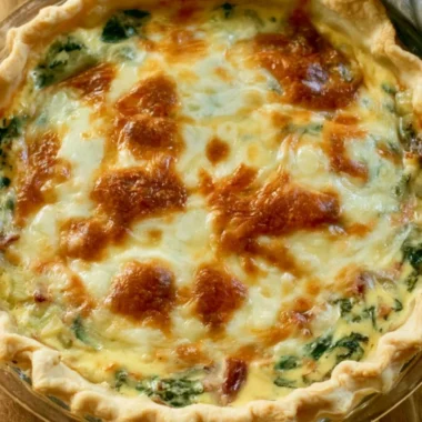 Cozy bacon spinach quiche slice on a plate, garnished with herbs.